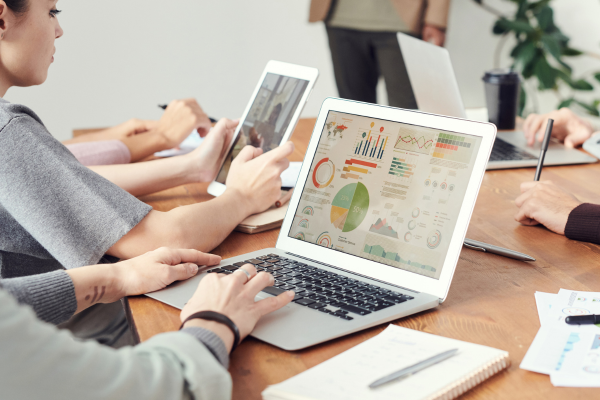 People at a desk with a tablet and laptop looking at graphs and reports.