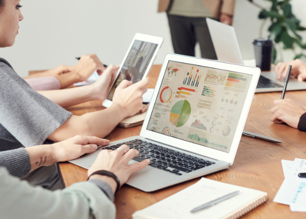 People at a desk with a tablet and laptop looking at graphs and reports.